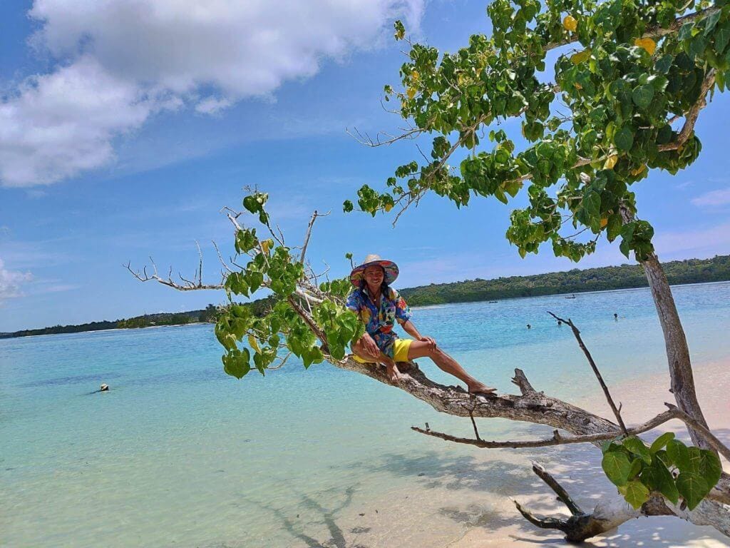 Un jeune homme malgache, assis sur un arbre au bord de l'eau. La mer est bleue et le paysage est magnifique.