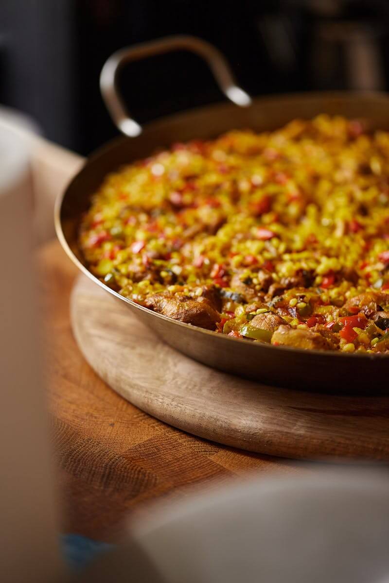 Photo by Manuel Mouzo A close-up of a delicious paella dish served on a rustic wooden table, showcasing vibrant ingredients.