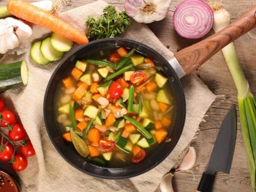 Minestrone ricetta della nonna con verdure fresche di stagione in pentola su tavolo rustico