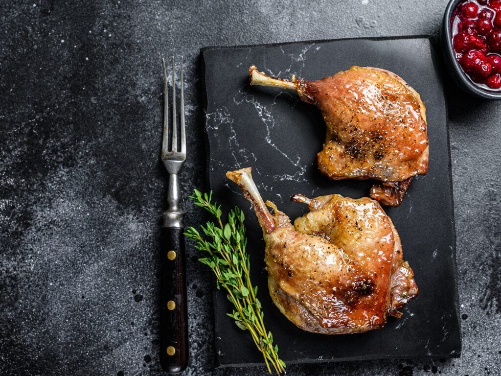 Recette cuisse de canard : viande caramélisée servie sur plateau d'ardoise avec garniture d'herbes aromatiques