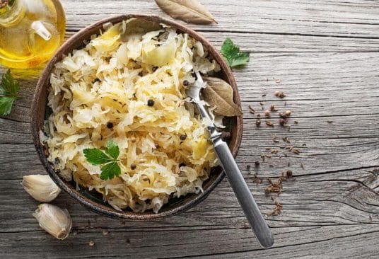 Plat de choucroute garnie alsacienne au mélange 5 baies, avec saucisses et viandes fumées, servi dans une cocotte.