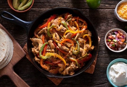 Plat de fajitas de poulet avec poivrons colorés, servi dans une poêle chaude avec tortillas et accompagnements.