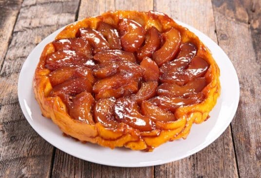 Tarte Tatin fondante aux pommes caramélisées sous une pâte dorée, saupoudrée de cannelle.
