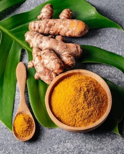 2 du curcuma frais à côté de curcuma en poudre posés sur une feuille