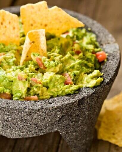 Mélange guacamole traditionnel servi dans un molcajete en pierre avec chips de maïs