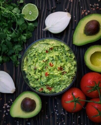 Mélange guacamole frais entouré de ses ingrédients : avocats, tomates, oignons et coriandre